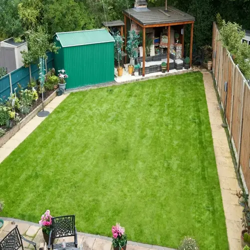 backyard garden featuring a lush green healthy lawn, green shed, wooden gazebo with seating area, and patio furniture surrounded by plants