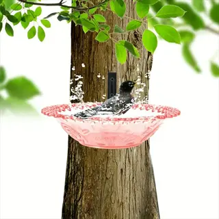 black bird splashing in water of pink hanging bird bath attached to tree trunk with green leaves