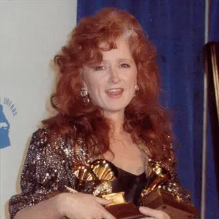bonnie curly holding grammy awards in front of blue event backdrop