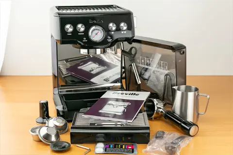 breville bambino mini espresso machine with accessories including portafilter, milk pitcher, and manual on wooden surface