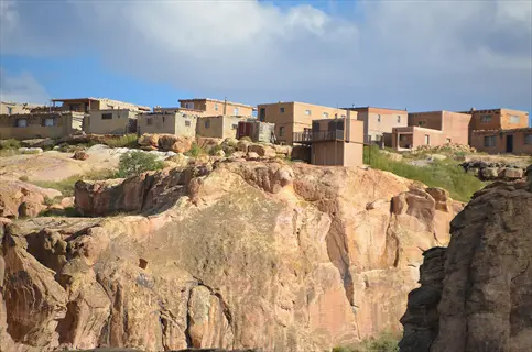 cliffside adobe architecture at acoma pueblo (sky city), new mexico, with desert rock formations under partly cloudy sky