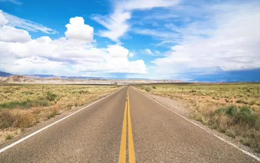 desert highway with grass median under blue sky with clouds