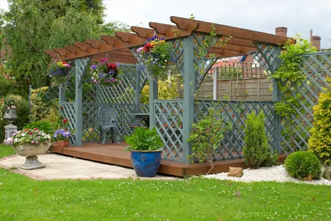garden shade structure: wooden pergola with lattice panels and deck in a landscaped garden, featuring hanging baskets, potted plants, and manicured greenery