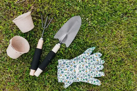 gardening tools on grass: flat head garden spade, garden fork, paper pots, and floral print gloves