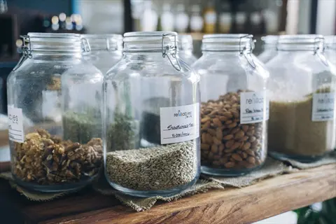 glass mason jars with metal clamp lids on a wooden shelf storing various seeds and nuts, labeled with 'refillables' and 'sunflower seeds' text