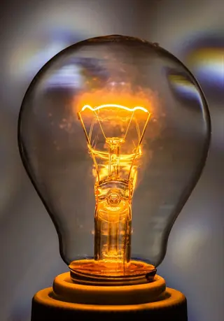 glowing incandescent grow bulb with warm orange filament light against soft bokeh background