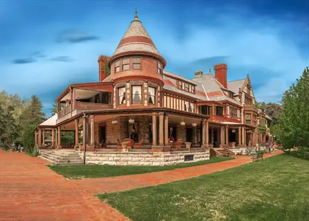 grand victorian-style mansion in a sunny garden location with brick walkways, green lawns, and partly cloudy sky
