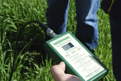 hand holding watermark soil probe tool (moisture meter) in grassy field for agricultural measurement