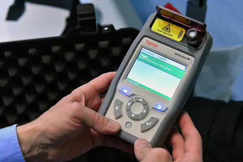 hands holding a thermo scientific portable light spectrometer with illuminated display showing text and optical sensor component