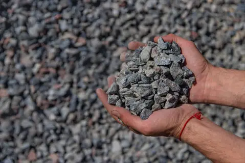 hands holding crushed granite gravel against a backdrop of more gravel