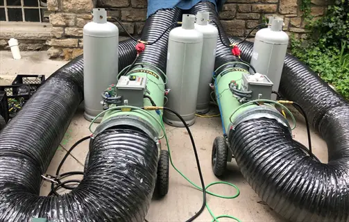 industrial heat treatment pest control equipment with propane tanks and ducting systems outdoors near stone wall