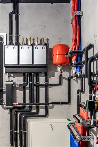 industrial hydronic greenhouse heating system control panel with color-coded pipes, pressure tank, and monitoring gauges