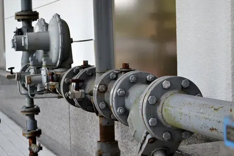 industrial water pressure valve assembly with rusted metal pipes, flanges, and control mechanisms mounted on an outdoor wall