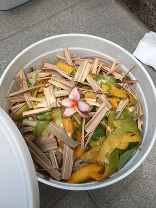 kitchen bokashi bucket filled with fruit peels, dried leaves, and topped with a decorative flower