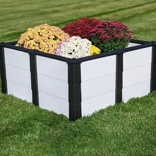 large outdoor resin planter box with black and white trim holding colorful chrysanthemum flowers on a grassy lawn