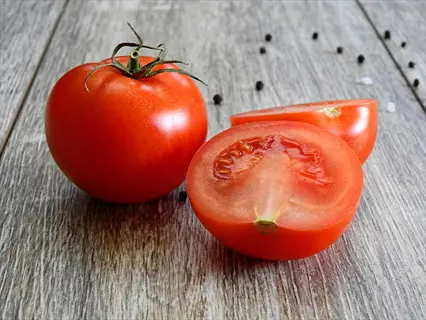 large red tomato slice with whole tomato on a wooden surface