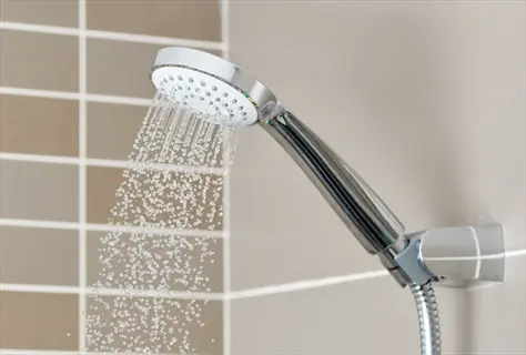 low-flow showerhead bathroom: water stream from a modern showerhead against a tiled wall, illustrating water-efficient home upgrades