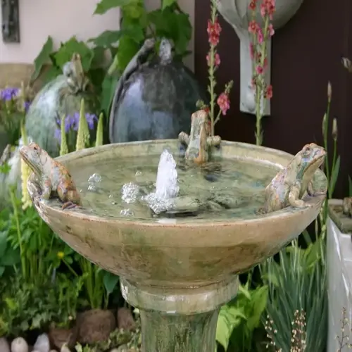 ornate bird bath garden with frog sculptures and blooming flowers