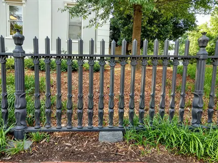 ornate black wrought iron garden fence with intricate scrollwork, surrounded by lush greenery and trees