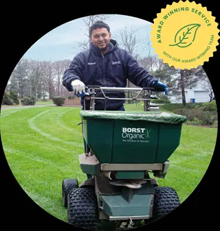 person operating a borst organic fertilizer lawn spreader on a grassy field with an award-winning service badge