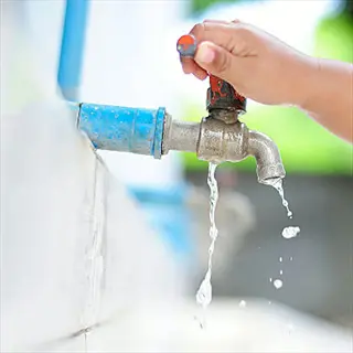 person turning off faucet: hand closing an outdoor tap with water dripping, demonstrating water conservation by turning off taps while not in use