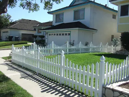 residential property with white vinyl picket fence surrounding a lush green garden