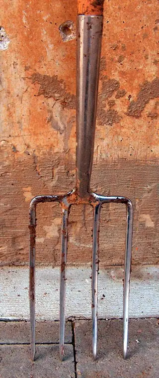 rusty metal digging fork with wooden handle against a weathered garden wall background