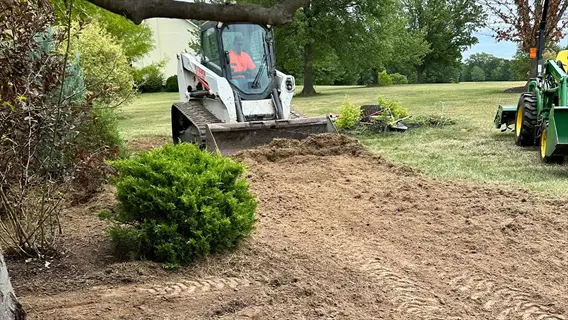 skid-steer loader preparing a slope with disturbed soil for slope seeding erosion control, operator visible in cab