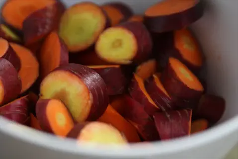 sliced purple dragon carrots in a white bowl, showing vibrant purple skin with bright orange flesh