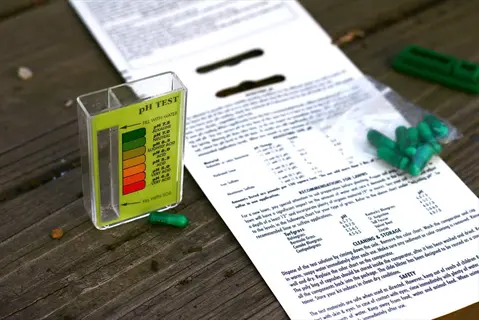 soil ph test kit components: transparent ph meter with color scale, instruction sheet, and green capsules on wooden surface - soil ph test kit