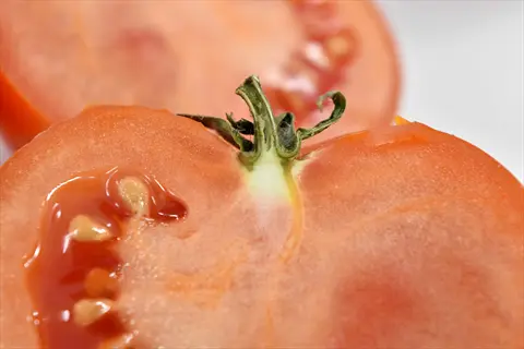 tomato seeds closeup in a freshly sliced red tomato with visible stem attachment