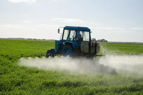 tractor-mounted sprayer applying pesticide spray to lush green agricultural field under sunny sky