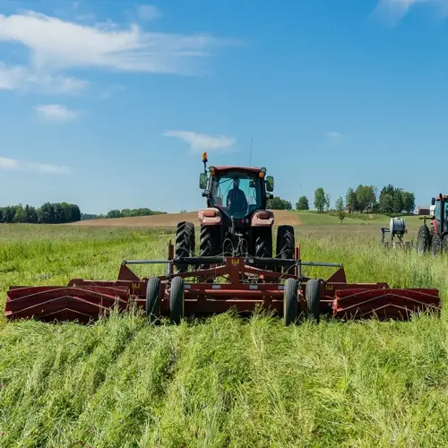 tractor working in a lush green farm cover crop field under clear blue skies, with another tractor visible in the background