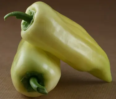 two ripe sweet banana yellow peppers with green stems arranged on a brown textured surface