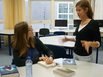 two women in a classroom with 'bitterblue' books; one signing, the other gesturing