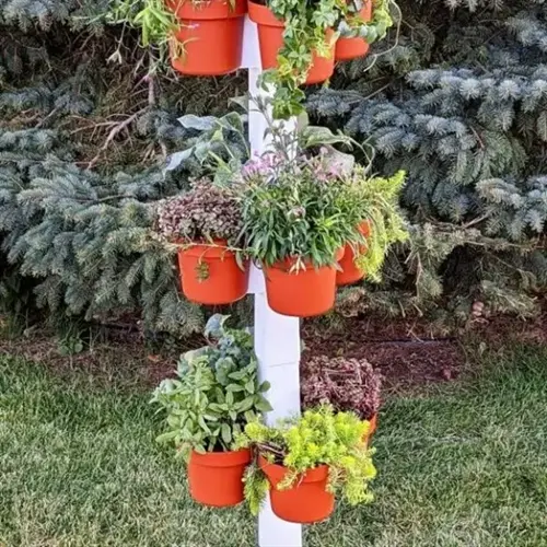 vertical stack of orange self watering planter herbs against evergreen trees