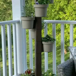 vertical stackable tiered planter balcony tower with multiple herb pots on a shaded porch with green trees in background