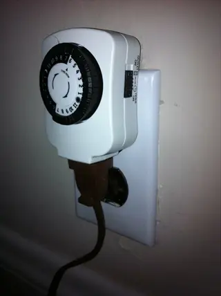 white mechanical outlet light timer with circular dial and brown cord plugged into a wall outlet