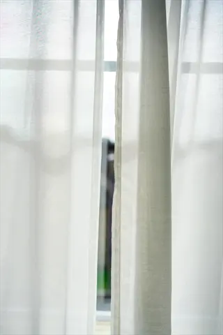 white sheer curtains framing a sunlit window with blurred outdoor background