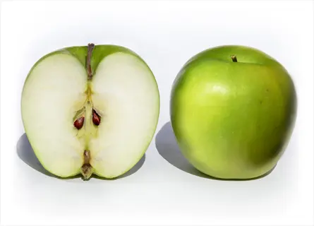 whole and halved granny smith apple showing seeds on white background