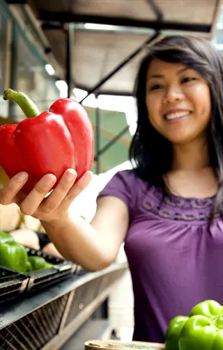 woman harvesting ripe peppers by holding a vibrant red bell pepper at a market stall
