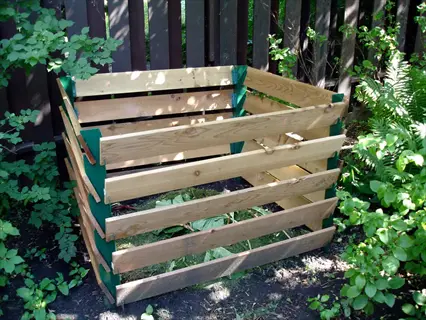 wooden compost bin with green trim surrounded by garden plants